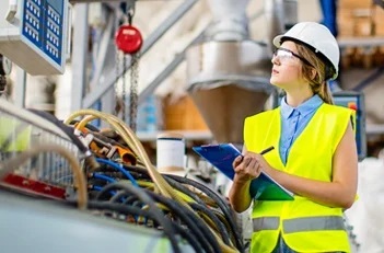Utility worker in a hard hat inspecting equipment and taking notes on a clipboard.